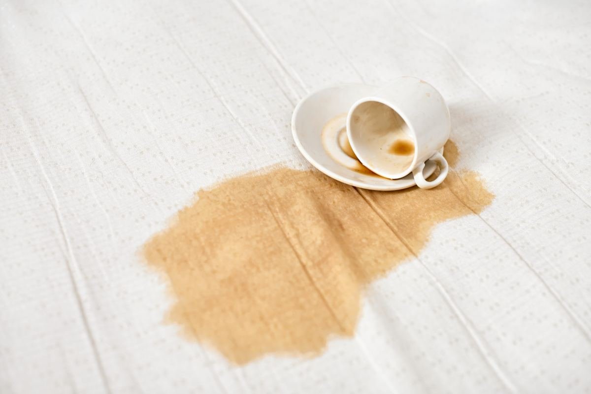 Xícara de café derramada sobre tecido claro, com a mancha já absorvida pelo tecido